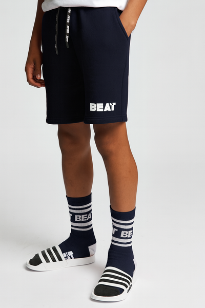 Person wearing navy shorts with 'BEAT' branding, matching socks, and Adidas shoes on a white background